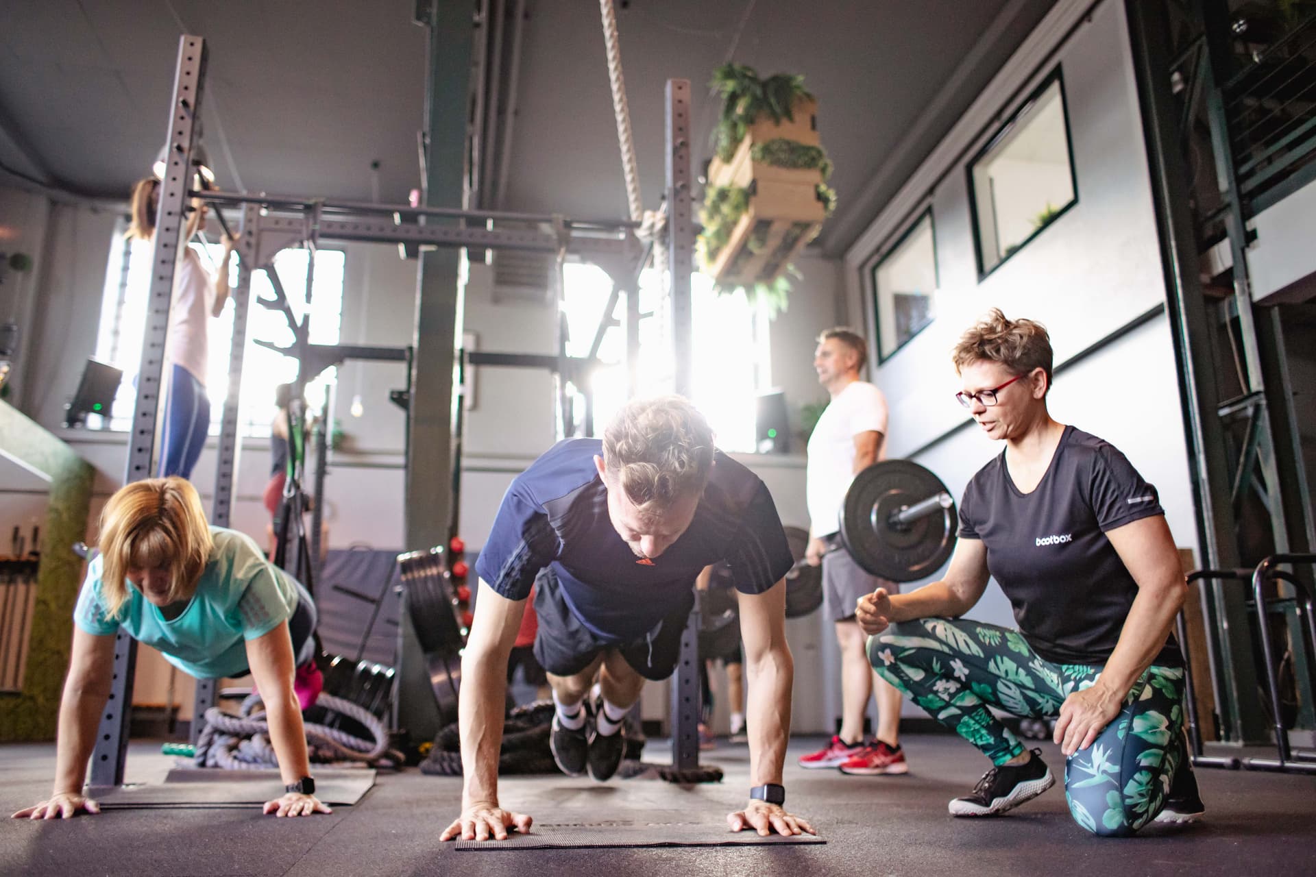 Trainerin korrigiert Kursteilnehmer im Slingtrainer beim Shape-Kurs.