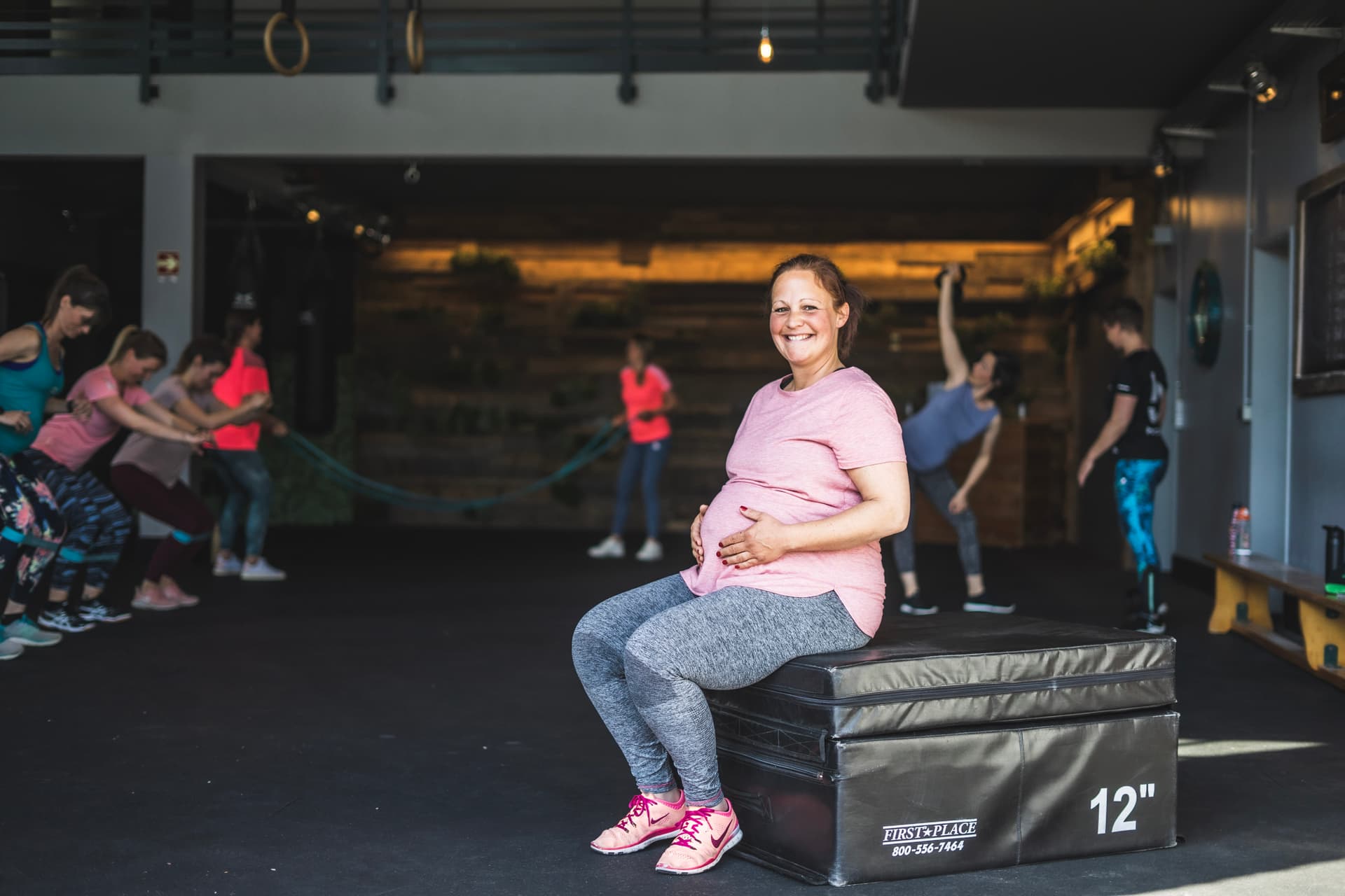 Eine Schwangere des Schwangerenkurses der Bootbox sitzt auf einer Fitnessbox und hält ihre Hände auf dem Bauch