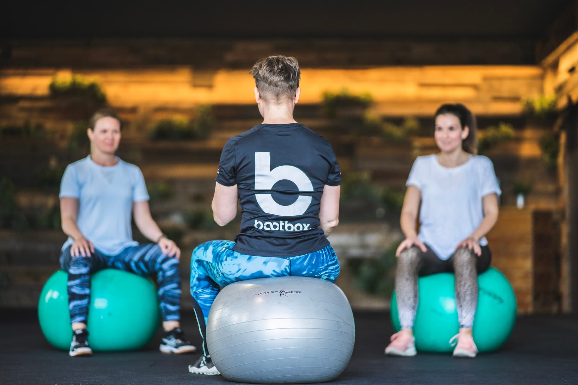 Zwei Frauen machen mit Fitnesstrainerin Nadine Schmitz Übungen auf Gymnastikball im Rückbildungskurs